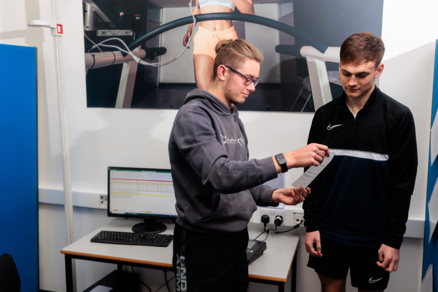Two students in a gym stood comparing fitness test results.