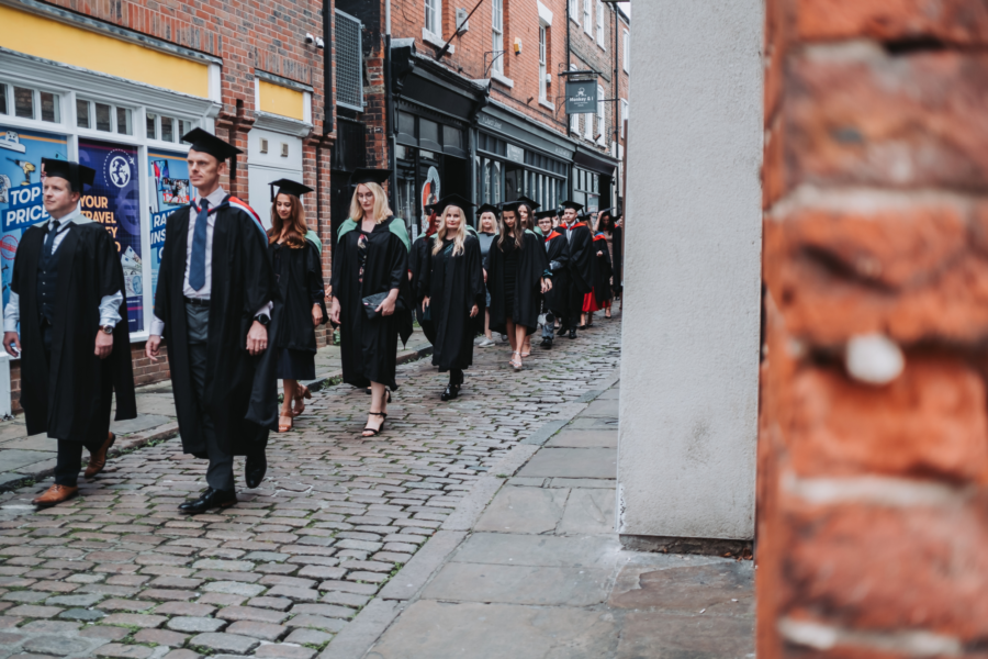 Student Graduates walk through the streets of Boston wearing caps and gowns.