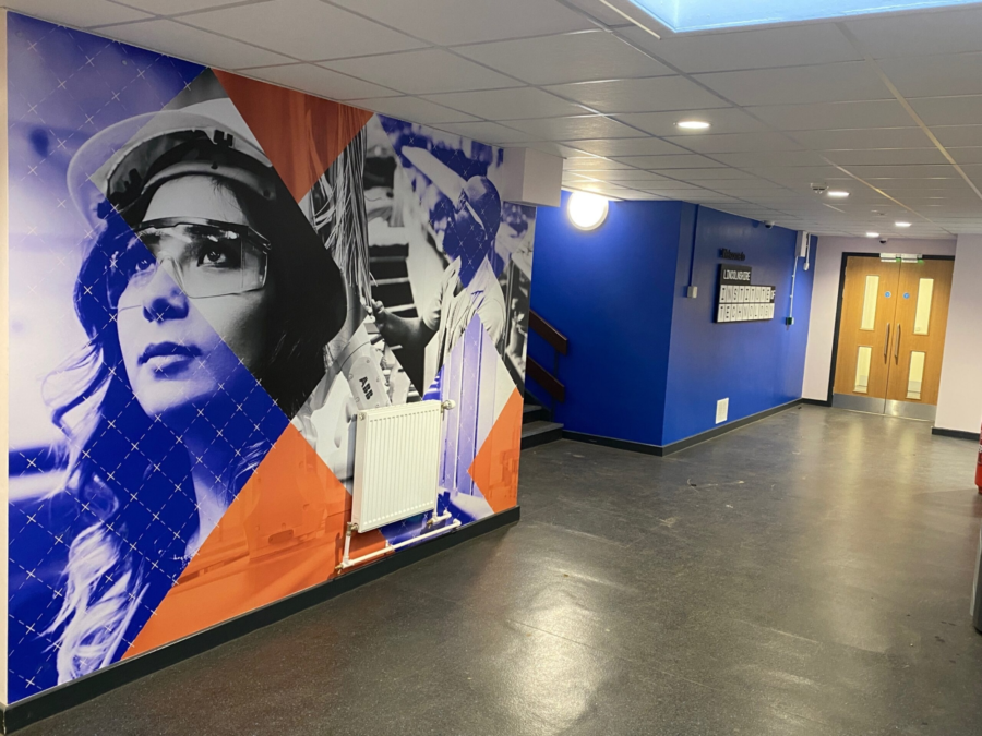 A corridor with a grey floor and multicoloured artwork on the wall.