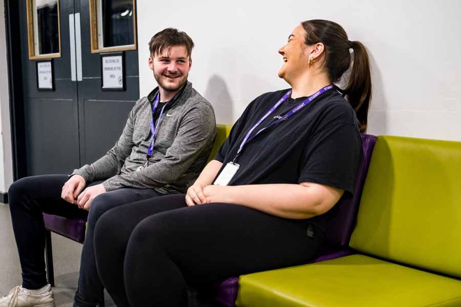 Students sat next to each other on a chair chatting.