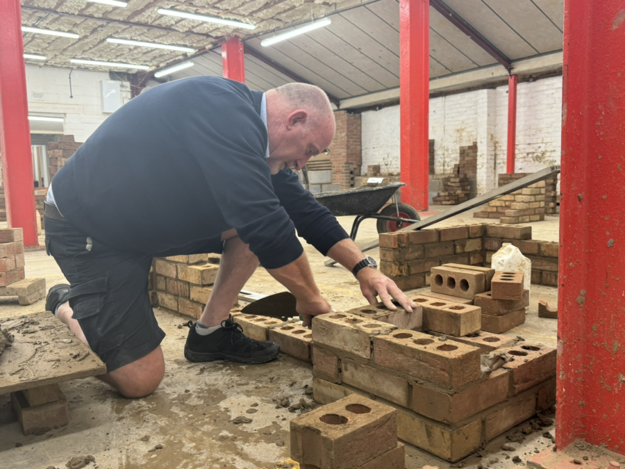 A person laying bricks on a wall in the bricklaying workshop.