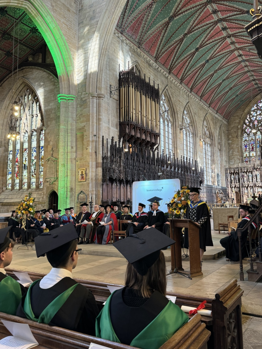 Image from Boston College Graduation 2025 - photo taken in Boston Stump, students sitting in Church pews facing away from the camera watching The Mayor of Boston's speech
